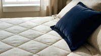 Cozy bedroom interior with navy blue pillow resting on quilted cream mattress near window, suitable for home decor, bedding, and lifestyle design projects.