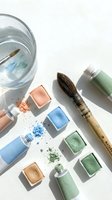 Watercolor paint cubes in blue, green and coral tones with brushes and water glass on white background for artistic projects and creative workshops.