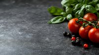 Fresh red cherry tomatoes on vine with water drops and green basil leaves on dark concrete background with copy space for food photography and menu design.