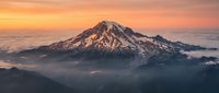 Majestic snow-capped mountain peak rising above clouds during golden sunrise with dramatic orange and pink sky creating breathtaking alpine landscape scenery.