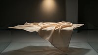 Draped beige fabric flowing across minimalist platform with dramatic spotlight lighting, creating elegant folds and shadows for contemporary design and artistic projects.