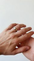 Close-up of hands wearing elegant gold wedding band ring on neutral background, symbolizing love, commitment and marriage ceremony celebration.
