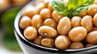 Fresh soybeans in black ceramic bowl with green basil leaf garnish, macro food photography showing texture and natural sheen of legumes.