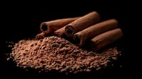 Aromatic cinnamon sticks on pile of ground cocoa powder against dark background, macro food photography with dramatic lighting and rich texture.
