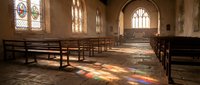 Historic church interior with wooden pews and colorful stained glass windows casting rainbow light patterns on stone floor for worship and spiritual themes.