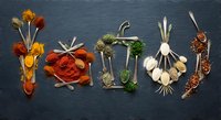 Colorful spices and herbs arranged to spell SPICY on dark slate background for culinary cooking and seasoning concepts.