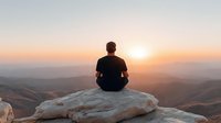 Man meditating on mountain rock at sunrise with peaceful valley landscape view. Mindfulness wellness retreat outdoor adventure spiritual journey.