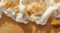 Gentle ocean wave washing over golden sand beach with white foam creating natural pattern and texture in warm sunlight. Perfect for travel designs.