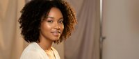 Young African American woman with curly hair smiling confidently in cream sweater, professional portrait for business and lifestyle content.
