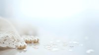 Delicate white lace fabric with scattered pearl beads on soft neutral background for wedding and bridal design projects.