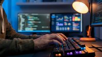 Software developer coding at night with multiple monitors displaying programming code and data analytics in modern workspace with ambient lighting.