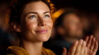 Smiling woman with glowing skin in warm ambient lighting, expressing joy and contentment while watching performance or event in theater atmosphere.