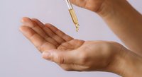 Woman applying facial serum oil from dropper bottle onto palm for skincare routine and beauty treatment on light background.