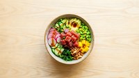 Fresh poke bowl with salmon, avocado, edamame and vegetables served in wooden bowl on light wood background for healthy dining menu design.