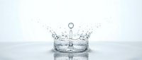 Water crown splash with droplets frozen in motion creating elegant liquid sculpture on reflective surface against clean white background.