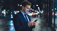 Young professional businessman in suit using smartphone on city street at night with bokeh lights background for business communication concepts.