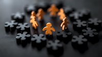Orange wooden figure standing out among black puzzle pieces on dark surface representing leadership and uniqueness in business teamwork.