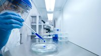 Scientist in protective gear conducting laboratory research with pipette and petri dish in modern sterile medical facility for scientific analysis.