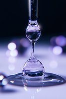Mesmerizing water drop collision captured in purple hues creating hourglass shape with bokeh background, frozen moment of liquid dynamics on reflective surface.