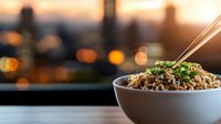 Delicious Asian noodle bowl with chopsticks against blurred city skyline at sunset. Fresh herbs garnish steaming ramen in white ceramic bowl on wooden table.