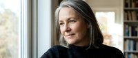 Mature woman with long gray hair and fair complexion gazing thoughtfully out window indoors, suitable for lifestyle, wellness, and aging gracefully concepts.