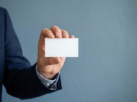 Businessman in dark suit holding blank white card against blue background for corporate branding and business card mockup designs.
