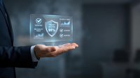 Businessman holding digital security shield with analytics icons and checkmarks, representing data protection and business compliance solutions.
