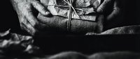 Elderly hands holding wrapped gift with twine and dried flower decoration in atmospheric black and white photography for holiday celebrations.