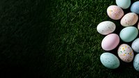 Pastel colored speckled Easter eggs arranged on dark green grass background with copy space, creating festive spring holiday composition.