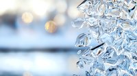 Frozen icicles with crystalline structure close-up against blurred winter background, natural ice formation with transparent texture and light reflections.
