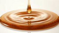 Amber liquid drop falling into circular ripple pool on neutral background, isolated for design use.