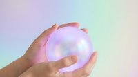 Hands holding glowing orb with soft rainbow light effects on pastel gradient background for spiritual wellness and energy healing concepts.