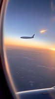 Silhouette of passenger aircraft seen through airplane window during sunset flight with meteor or shooting star streaking across sky, dramatic aerial view.