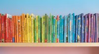 Colorful children books arranged in rainbow order on white shelf creating vibrant educational library display for learning and reading development.