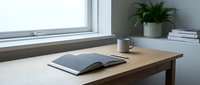 Wooden desk with open book and coffee mug by bright window, minimalist workspace with potted plant and books on shelf for home office or study room design.