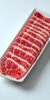 Fresh marbled beef slices arranged in row on white rectangular plate, showing rich red meat texture with white fat marbling pattern, suitable for food marketing.