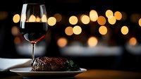 Grilled steak with red wine glass on elegant dining table with warm bokeh lights creating romantic restaurant atmosphere for fine dining experience.