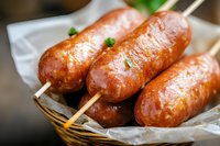 Grilled sausages on wooden skewers in wicker basket with parchment paper. Fresh cooked bratwurst ready to serve for barbecue party or outdoor dining.