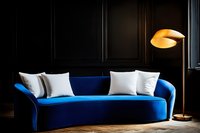Modern royal blue velvet sofa with white cushions in dark moody interior, illuminated by warm floor lamp light against black wall with moldings.