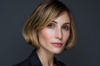 Professional blonde businesswoman with bob haircut in dark suit jacket against gray background for corporate headshot and business portrait use.