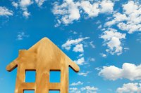 Wooden house silhouette against vibrant blue sky with white fluffy clouds. Minimalist real estate concept representing home ownership and property market.