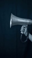 Hand holding vintage megaphone loudspeaker against dark background for communication and announcement concepts.