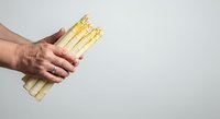 Close-up of male hand holding bundle of fresh white asparagus spears against neutral background for culinary and food styling projects.