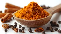 Ground turmeric powder in wooden spoon with black peppercorns and cinnamon sticks on rustic background, aromatic spices for healthy cooking and wellness.