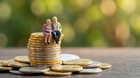 Miniature elderly couple sitting on stack of golden coins representing retirement savings, financial planning and pension fund investment security.