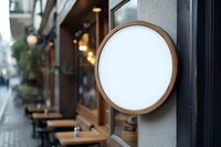Round wooden frame mockup with blank white space mounted on cafe exterior wall, perfect for restaurant branding and signage design.