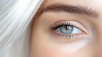 Close-up view of bright blue eye with long eyelashes, natural eyebrow and flawless skin showing professional makeup artistry and beauty concept.