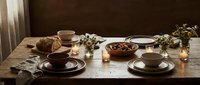 Cozy breakfast table setting with coffee cups, pastries and warm morning sunlight streaming through window creating intimate dining atmosphere for two people.