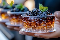 Hand holding a glass filled with cola or dark soda topped with fresh blueberries and mint leaves, carbonated beverage with ice cubes, refreshing summer drink for advertising and food styling.