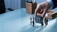 Business professional hand placing justice scales with miniature people figures on office desk representing legal consulting and corporate law services.